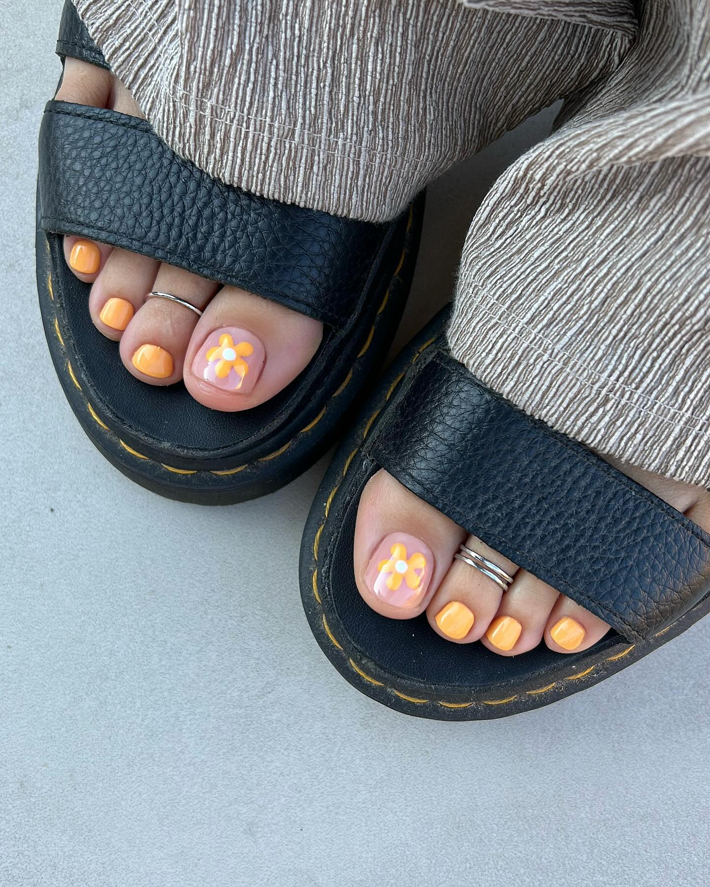 Orange and white floral pedicure on feet in black sandals