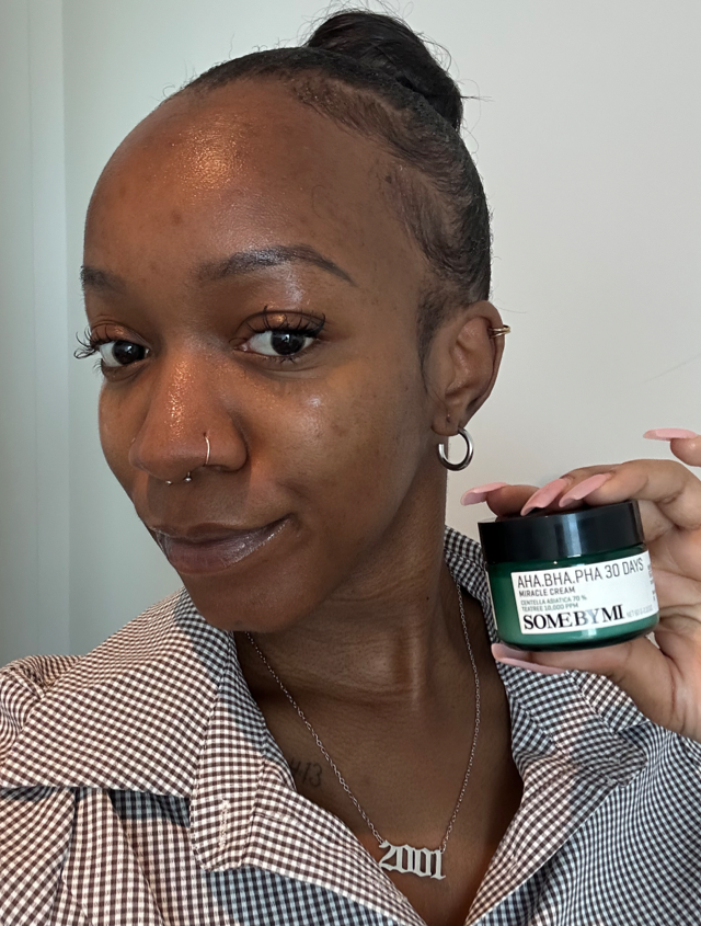 Someone holding up a SOME BY MI moisturiser with glowy, clear skin