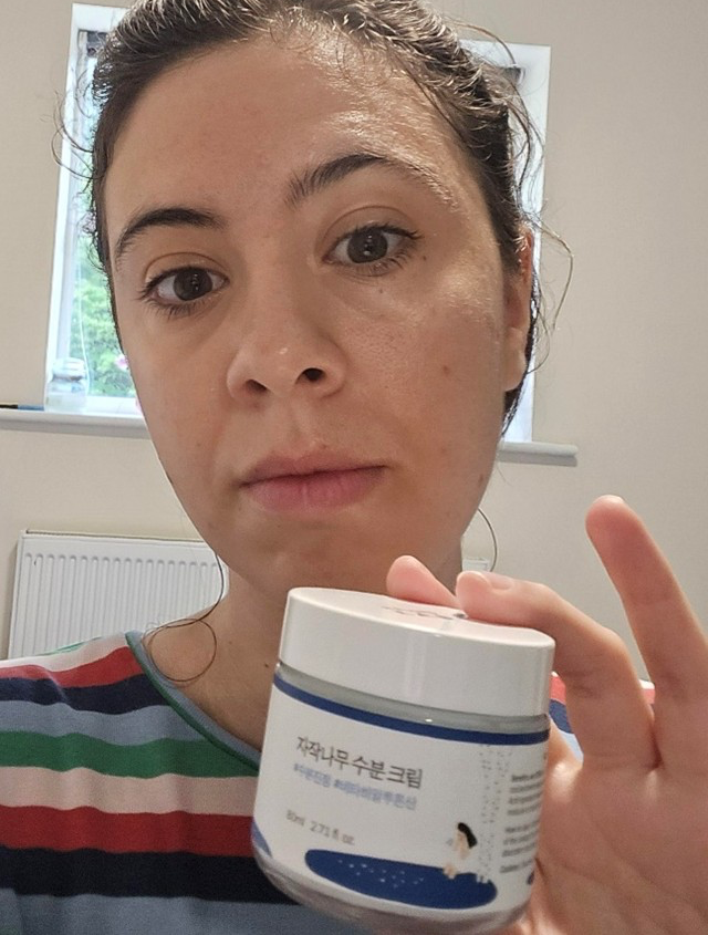 Someone holding a blue and white tub of moisturiser with clear skin