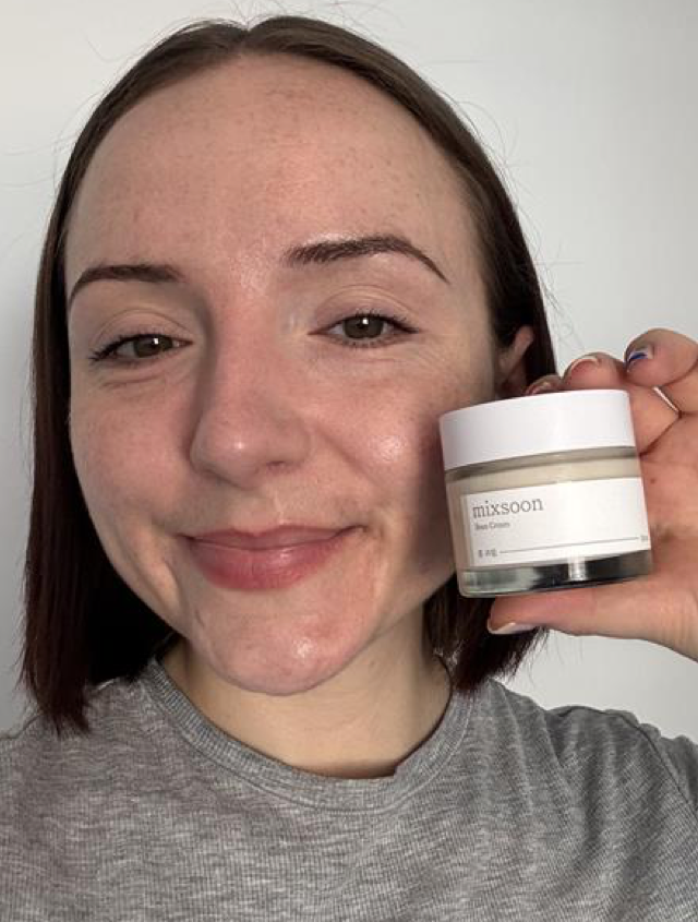 Someone holding up a tub of moisturising cream with clear, glowing skin