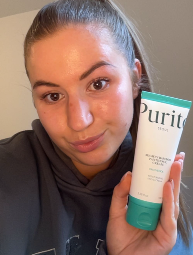 Someone holding a green and white tube of moisturiser with glowing skin