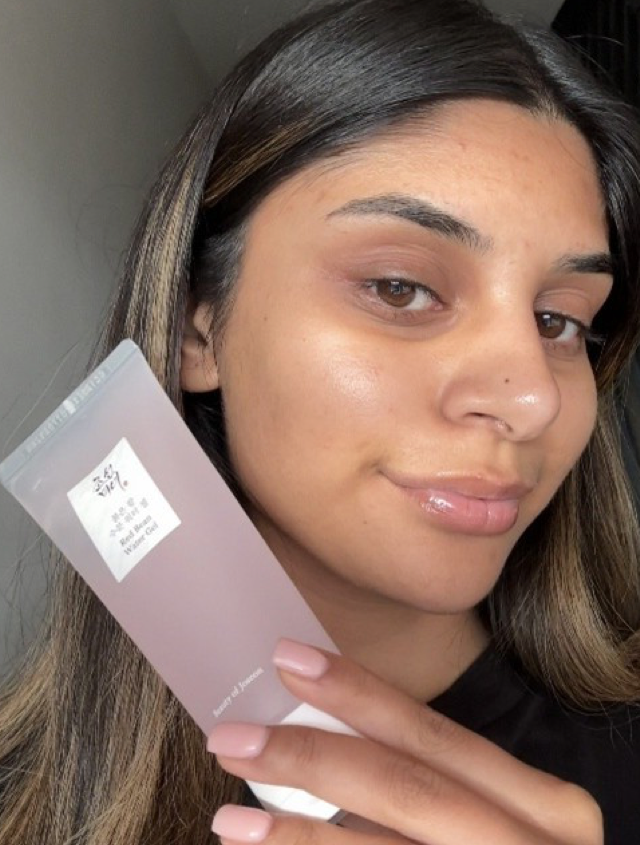 Someone holding up a Korean moisturiser to their face whilst smiling with glowing skin
