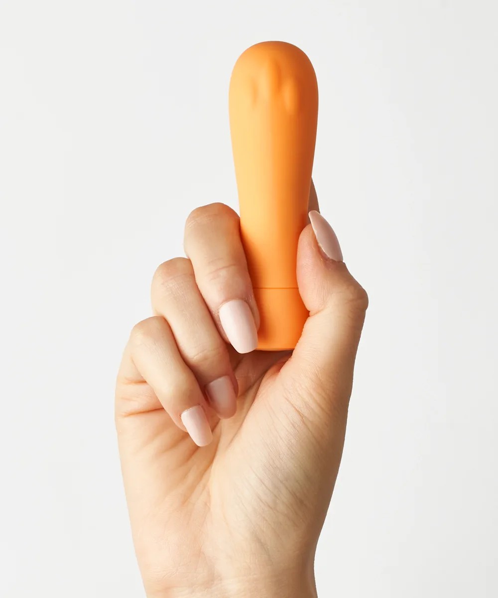 An orange bullet vibrator being held up by a hand on a white background