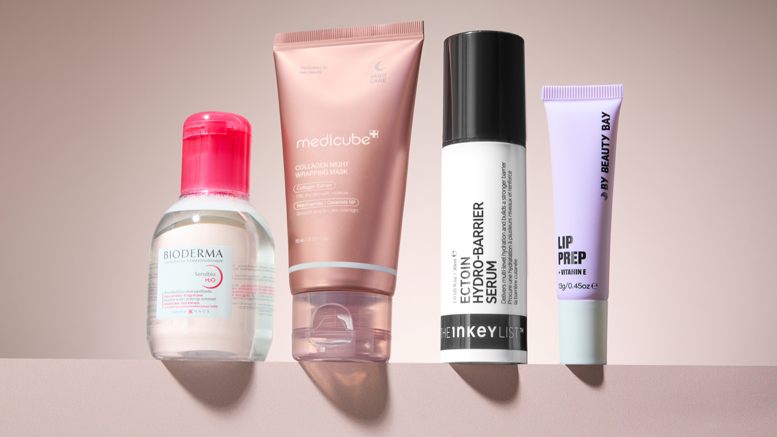 Four skincare products next to each other on a pink background