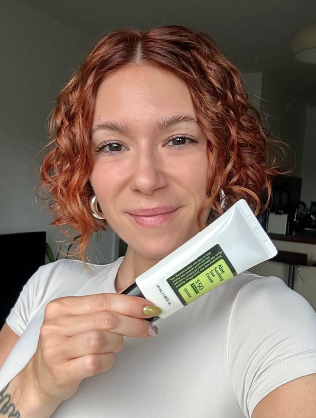 Someone holding the COSRX Aloe Soothing SPF 50 in a white and black tube with glowing skin