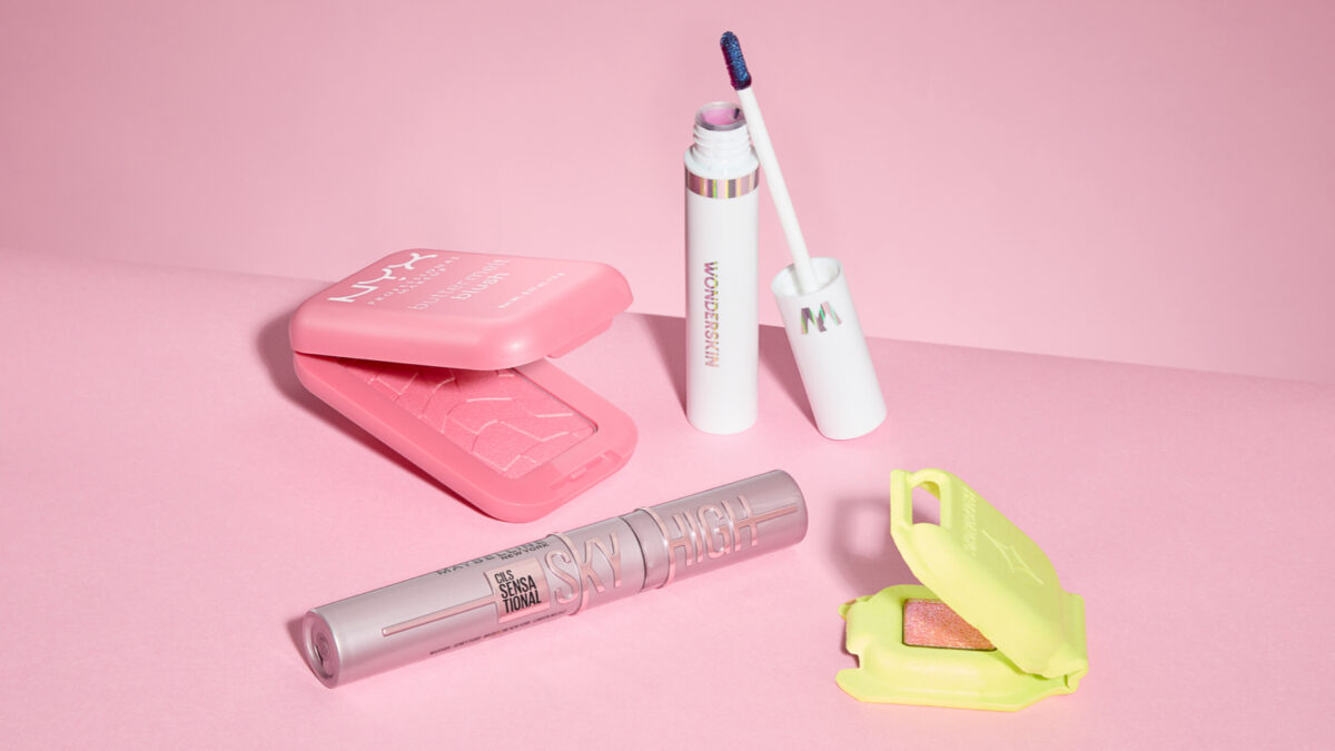 Four makeup products stacked next to one another on a pink background