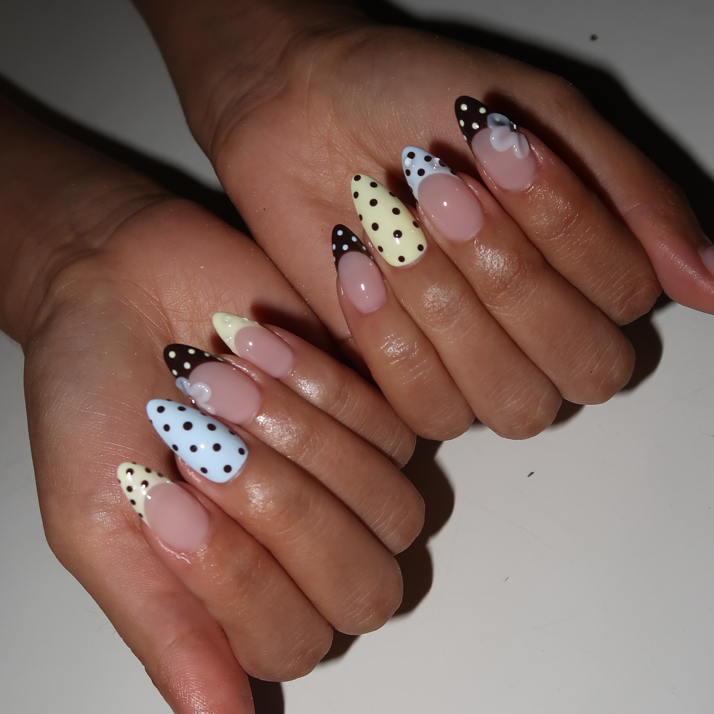 Two hands with polka dot nails in various different designs, in shades of yellow, blue, and brown