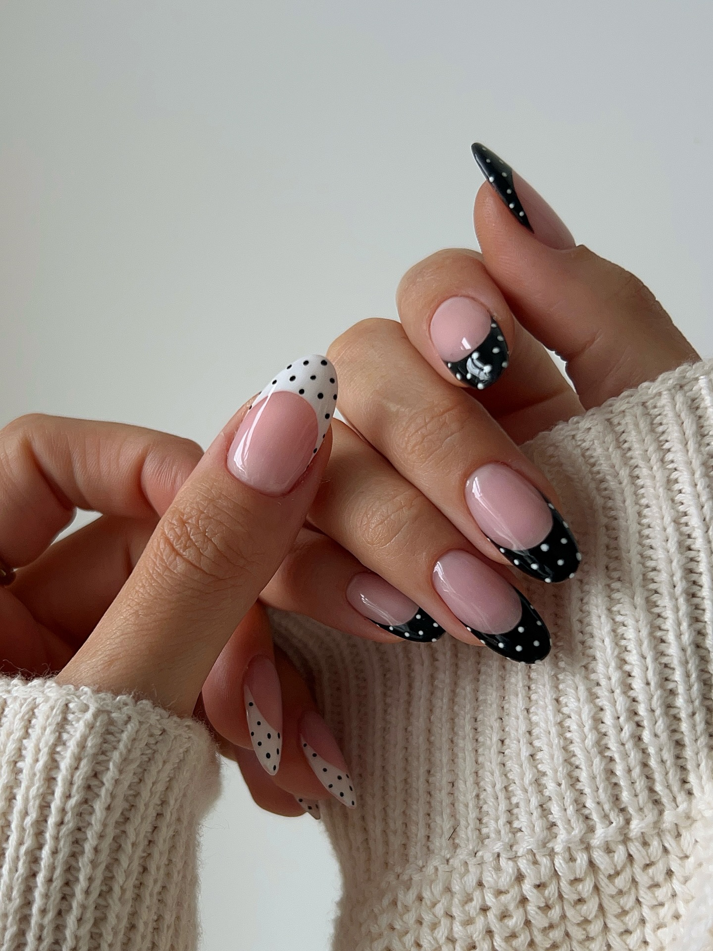 Two hands with opposite polka dot French tip nails in black and white