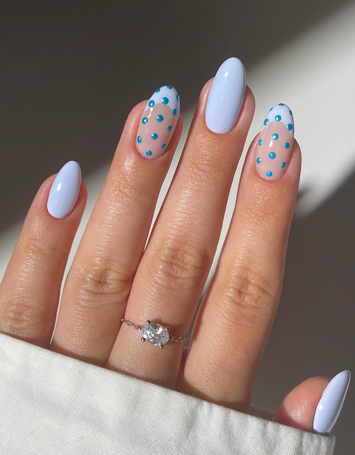 A hand with blue French tips and glittery blue polka dots on long nails