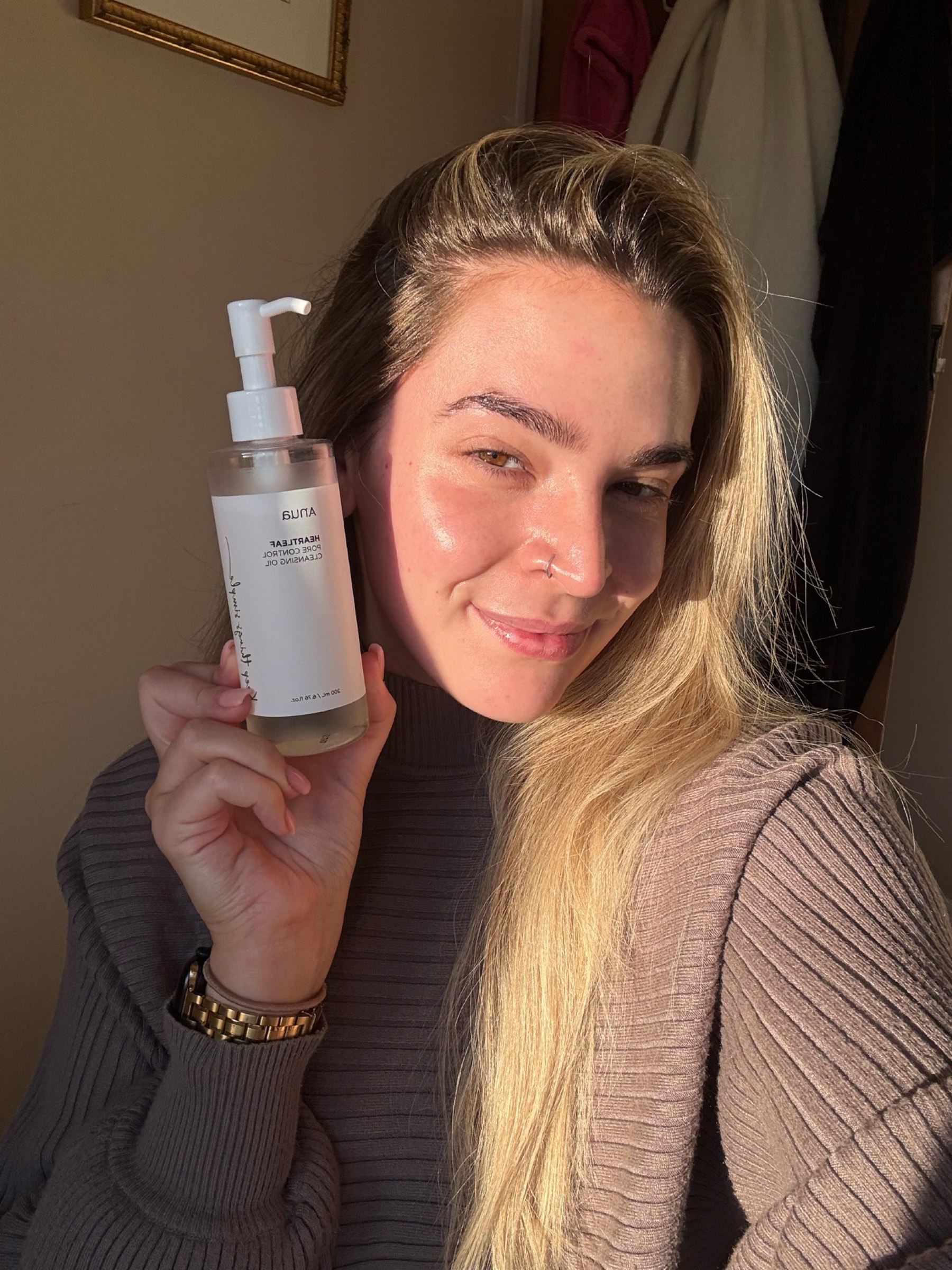 Someone holding the ANUA Cleansing Oil with glowing skin
