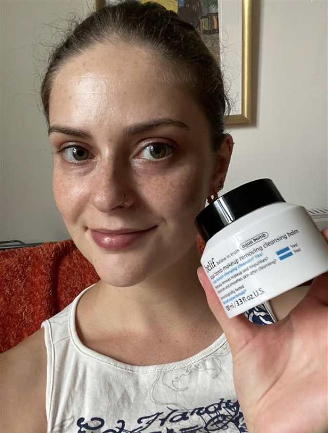 Someone holding the Belif cleansing balm in white and black packaging with clear, smooth skin