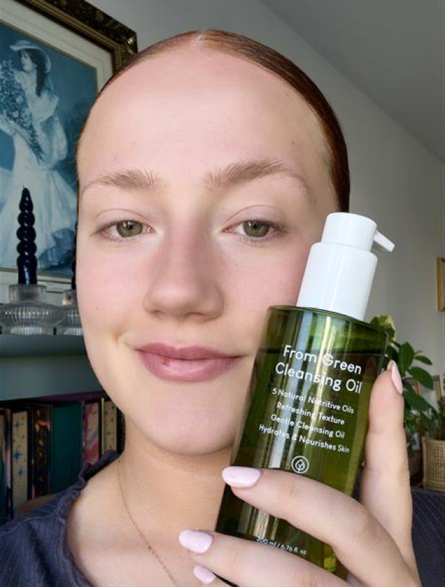 Someone holding the Purito Seoul cleansing oil in a green bottle with clear skin