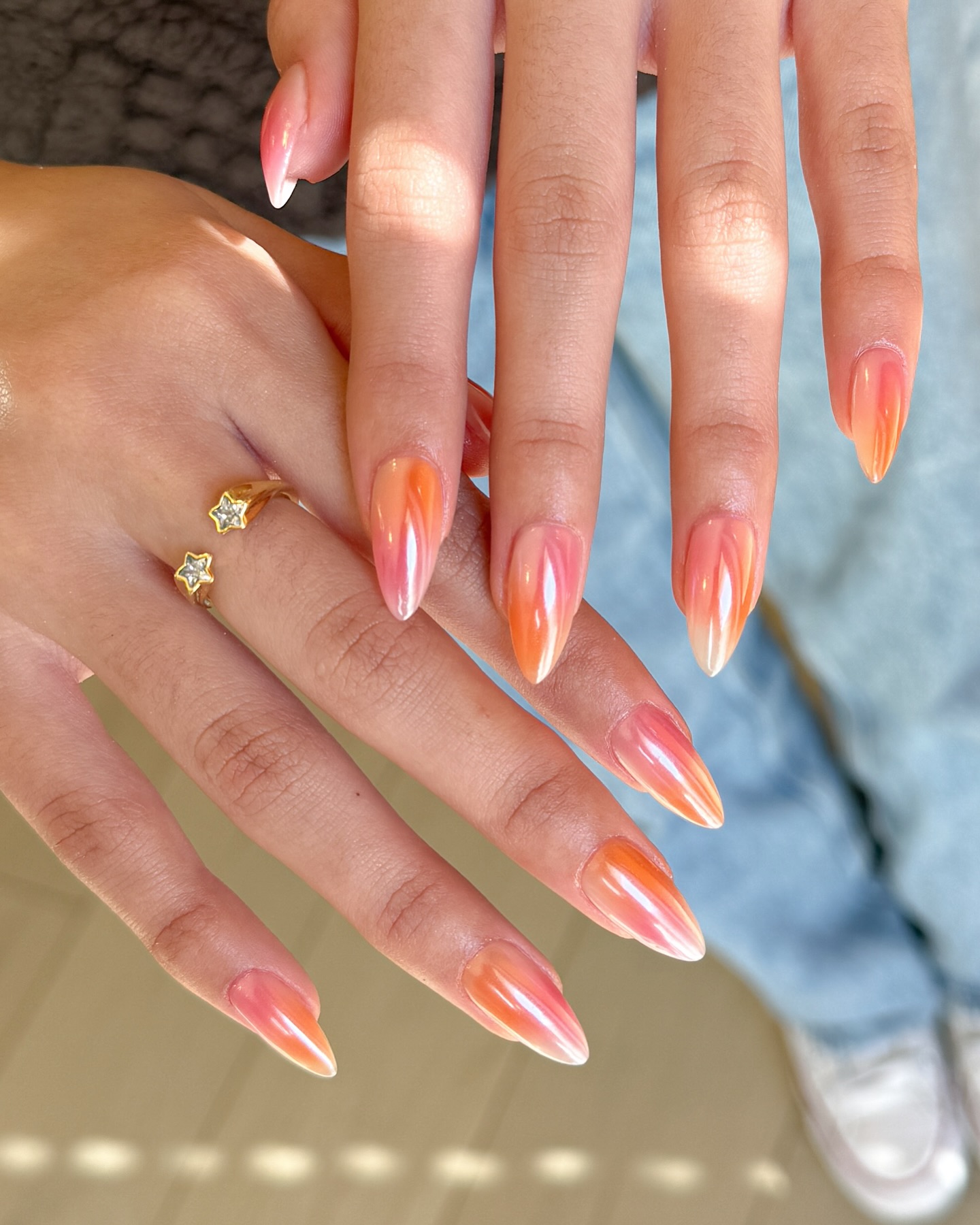 A close up of two hands with orange and pink chrome nails