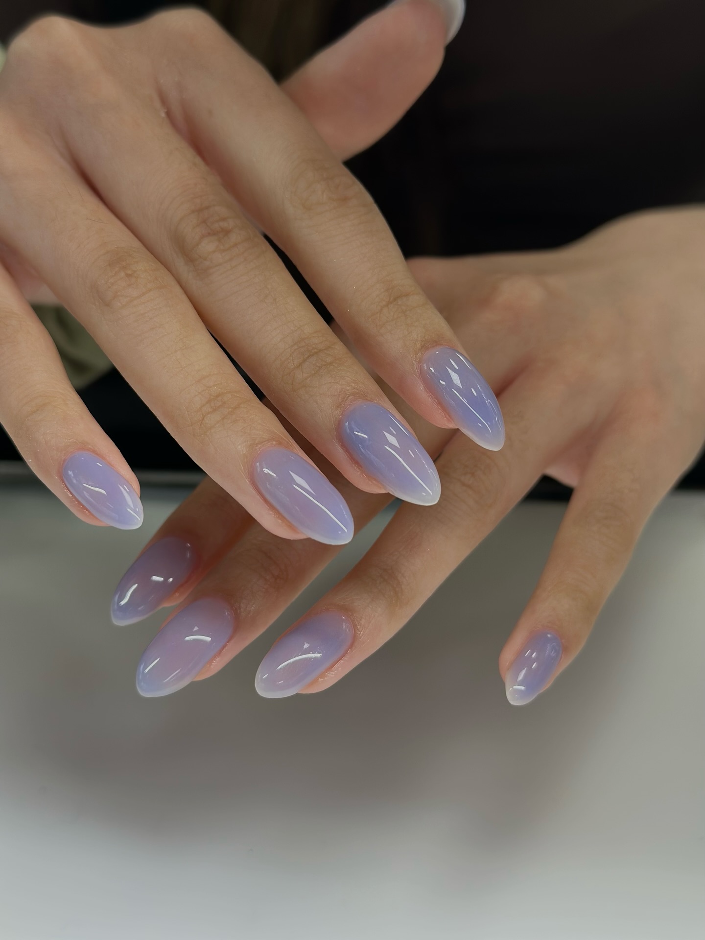 A close up of two hands with almond-shaped nails and a lilac jelly nail design
