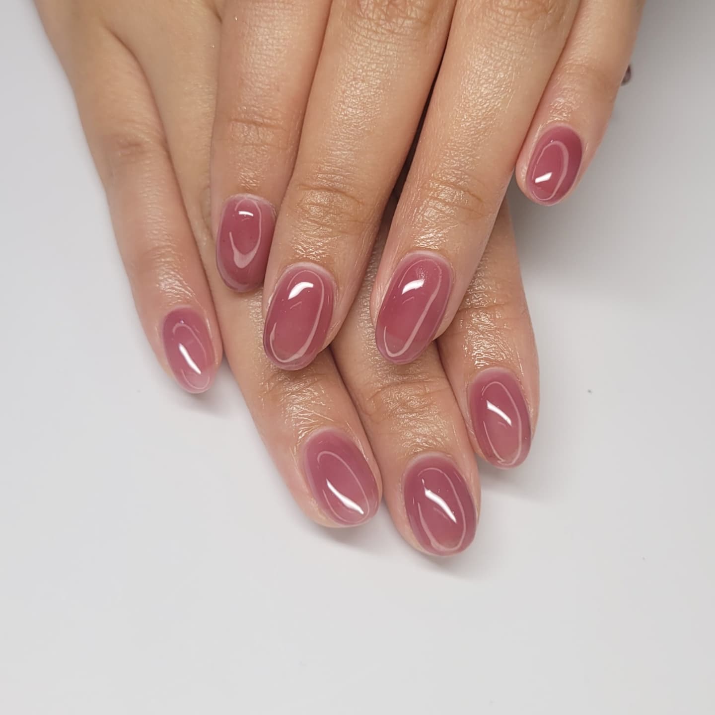 A close up of two hands with almond shaped nails featuring a pink nail design