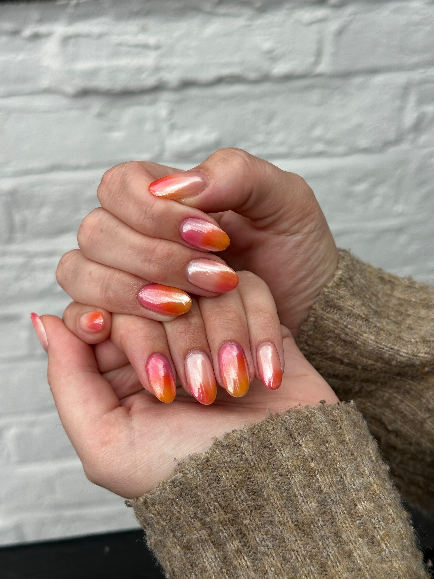 A close up of two hands with orange chrome nails