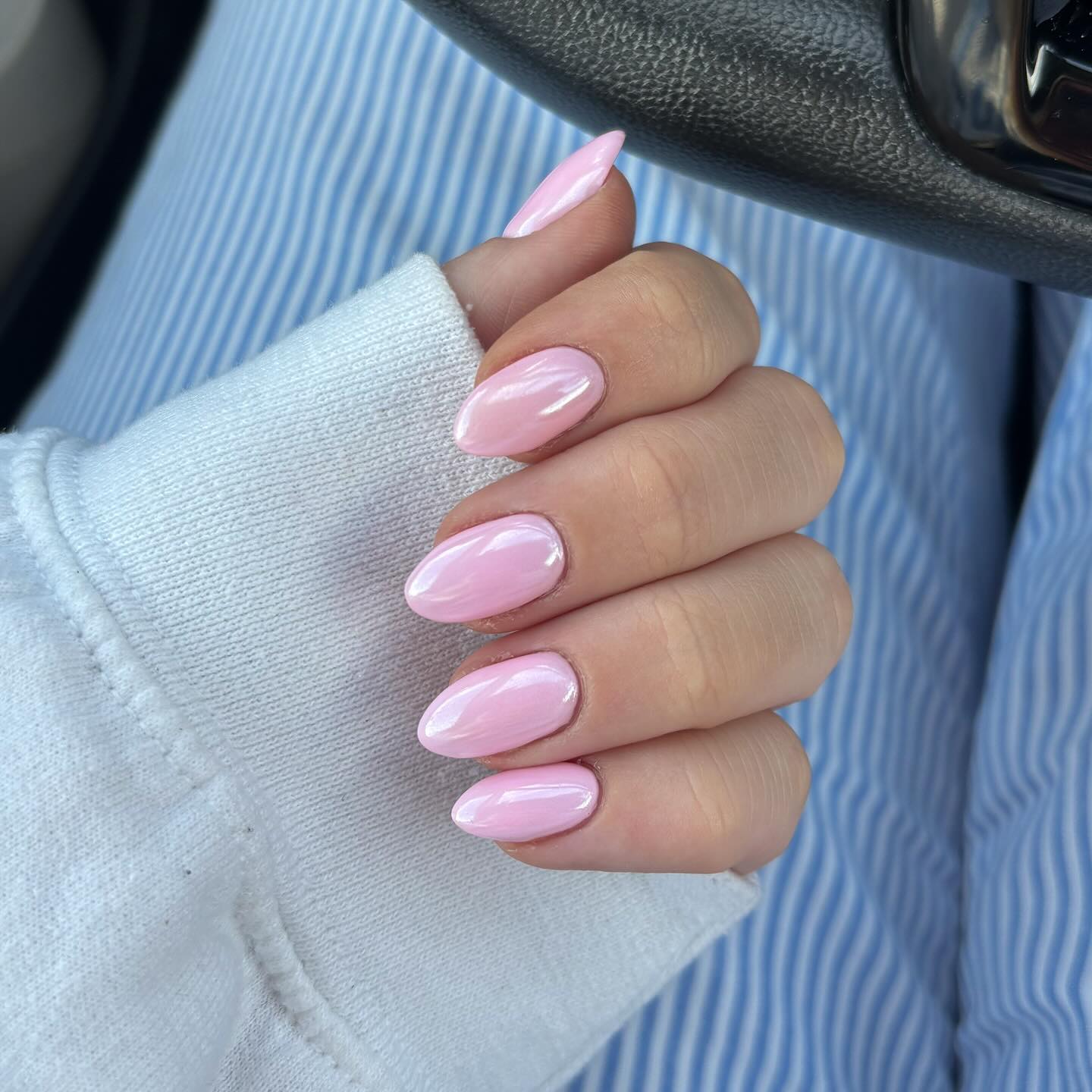 A close up of a hand with almond shapes nails featuring a baby pink chrome polish