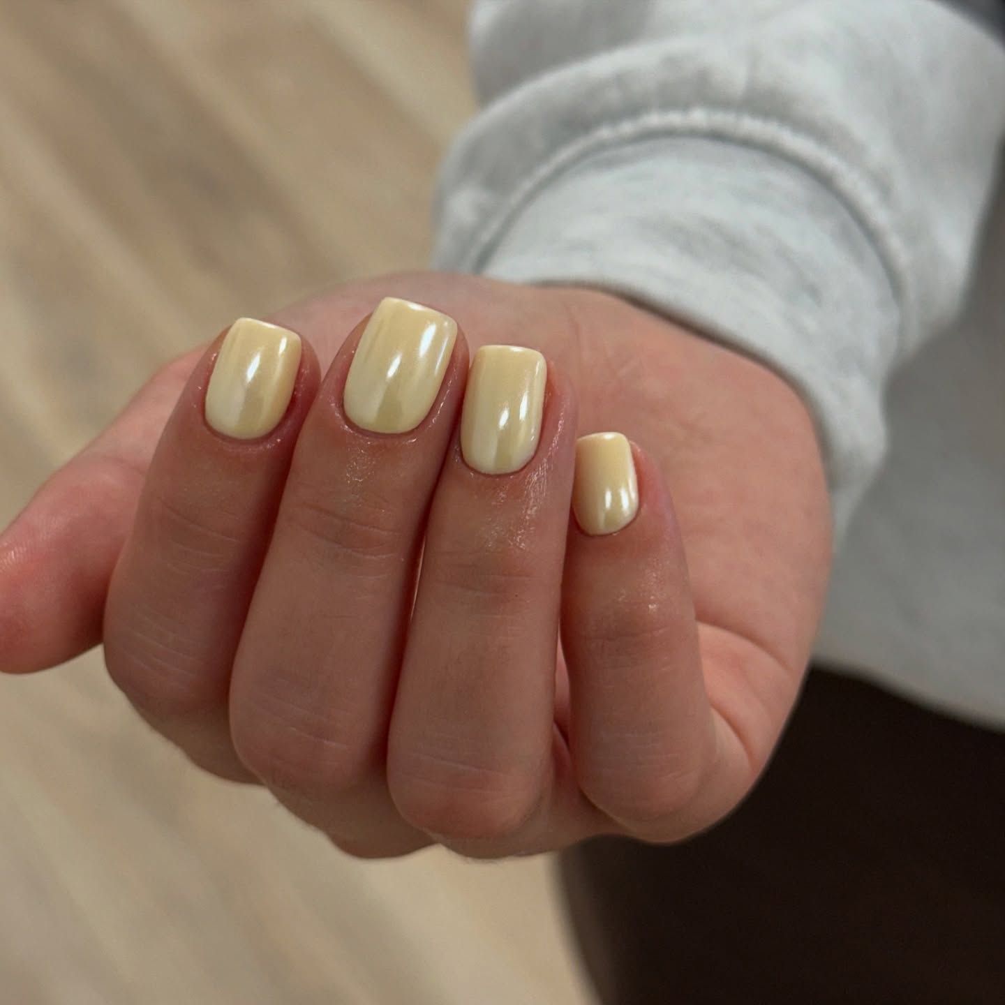 A close up of a hand with square nails and butter yellow chrome nails