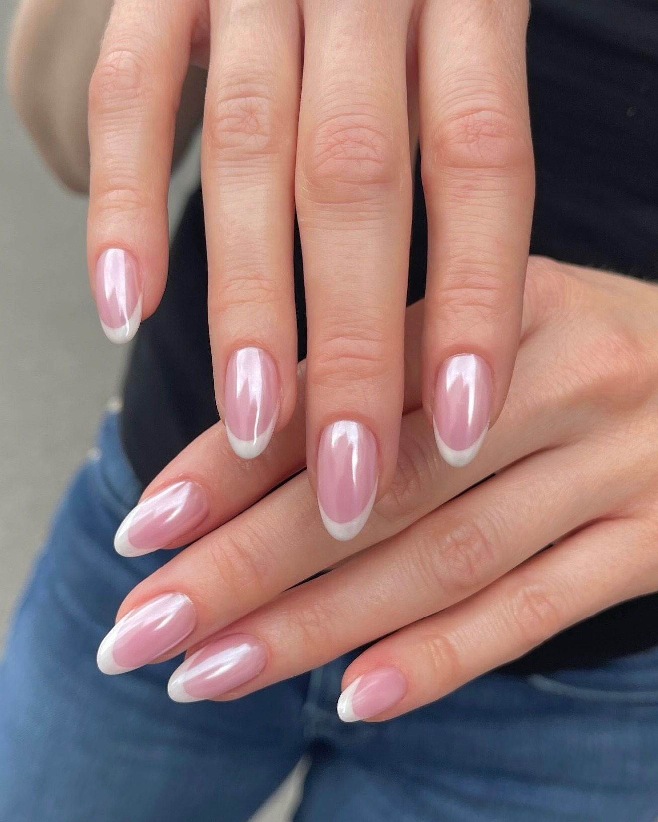 A close up of two hands with white French tip chrome nails