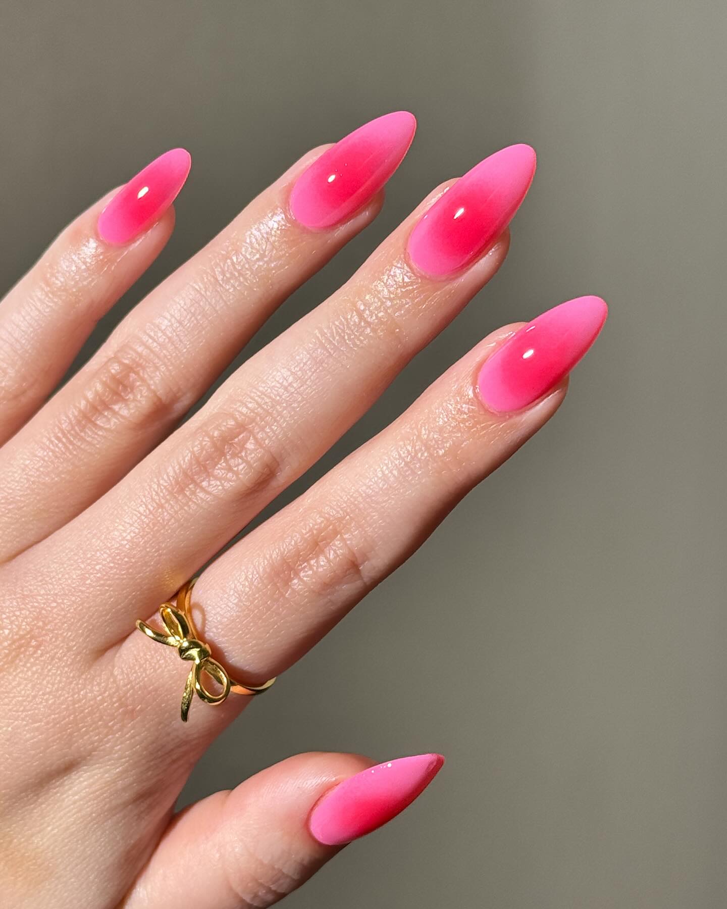 A close up of a hand with almond shaped nails with a pink nials