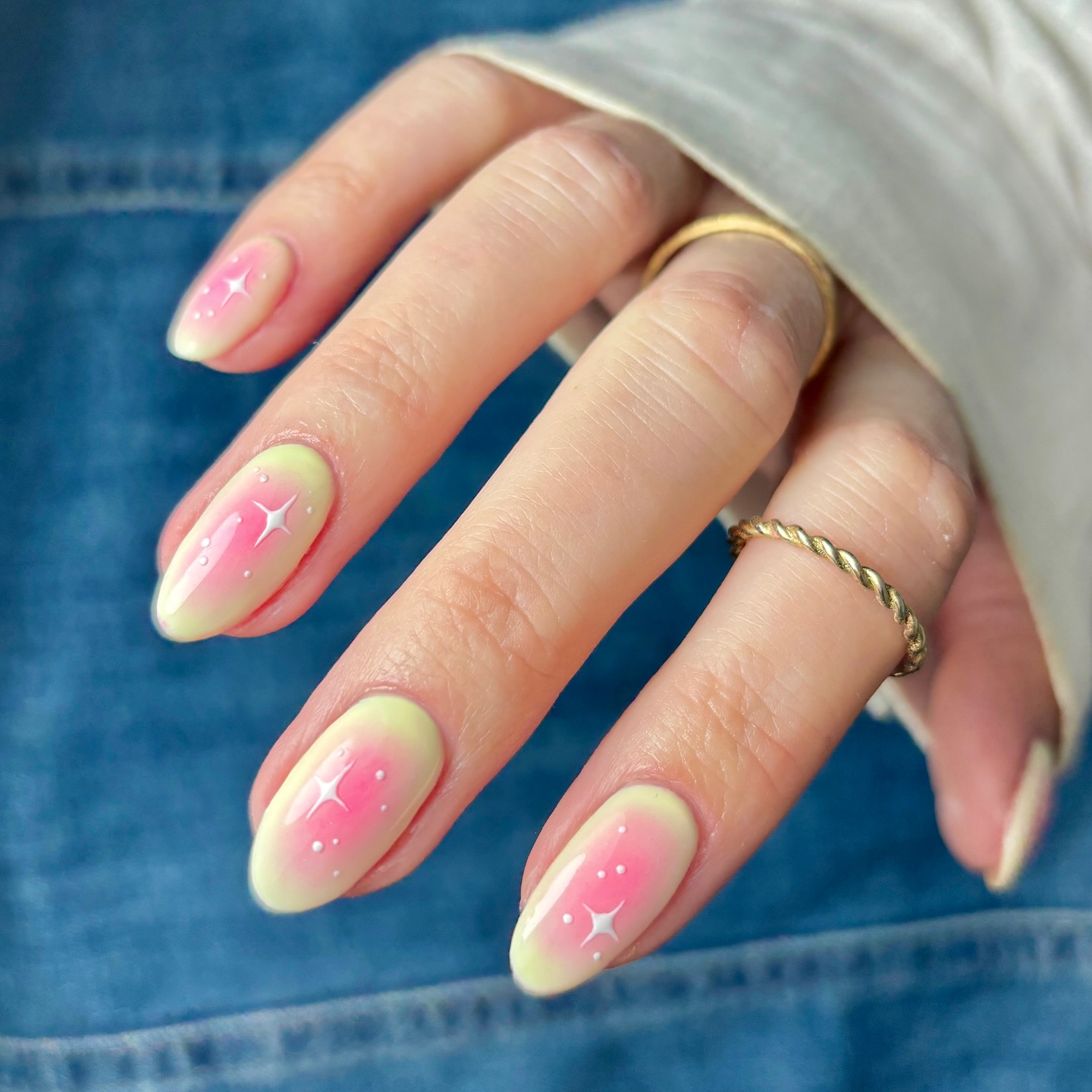 A close up of a hand with almond nails featuring a yellow base colour with a pink gradient centre and white sparkle details