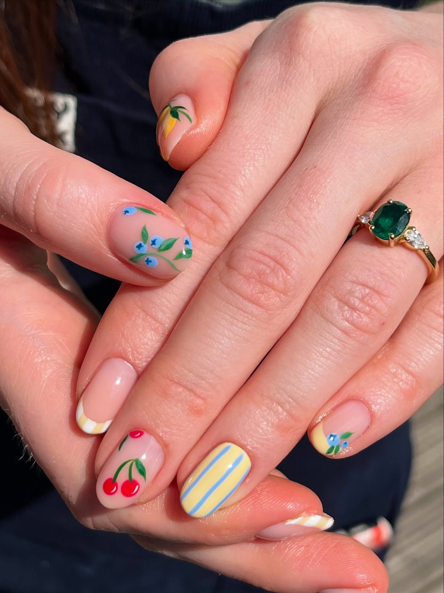 A close of up a hand with almond shaped nails featuring mini fruit designs