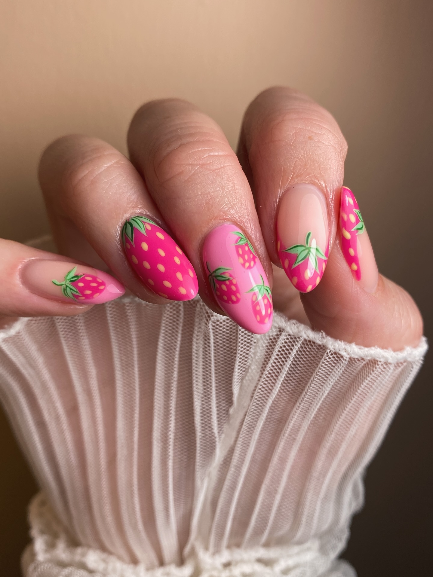 A close up of a hand with almond shaped nails featuring a pink strawberry design