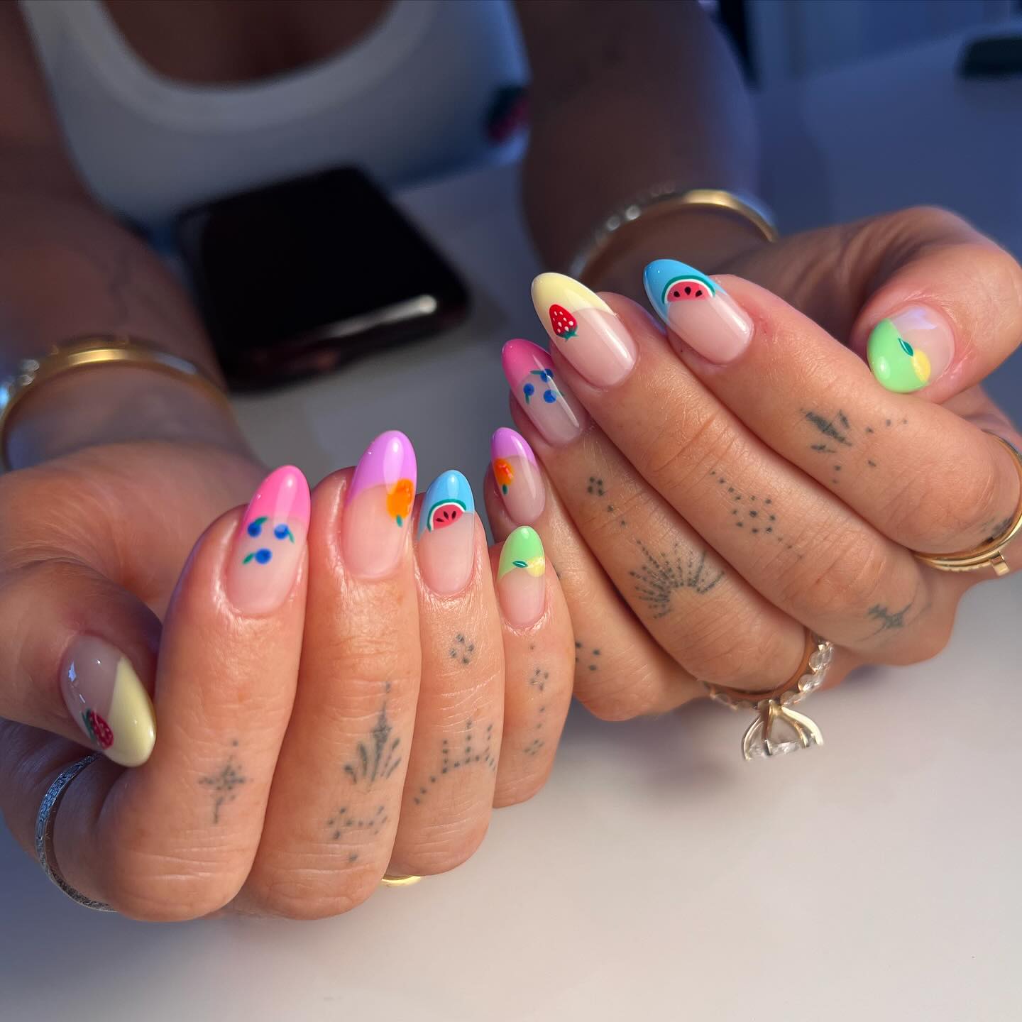 A close up of a hand with almond shaped nails featuring a micro fruit design