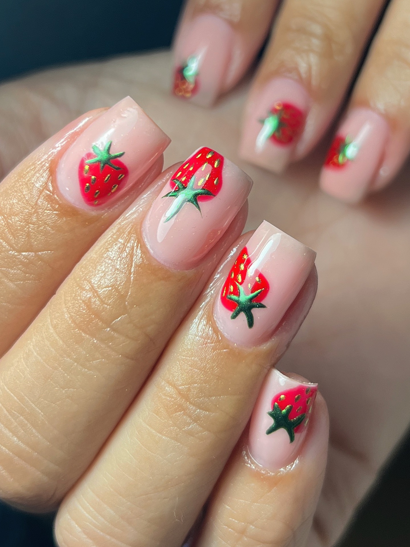 A close up of a hand with square nails featuring a neutral base with a strawberry design