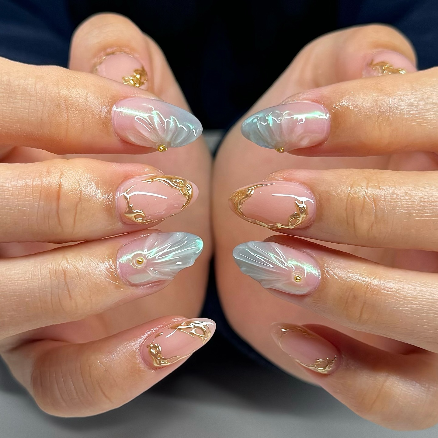 A close up of two hands with almond shaped nails featuring a blue and nude shell design