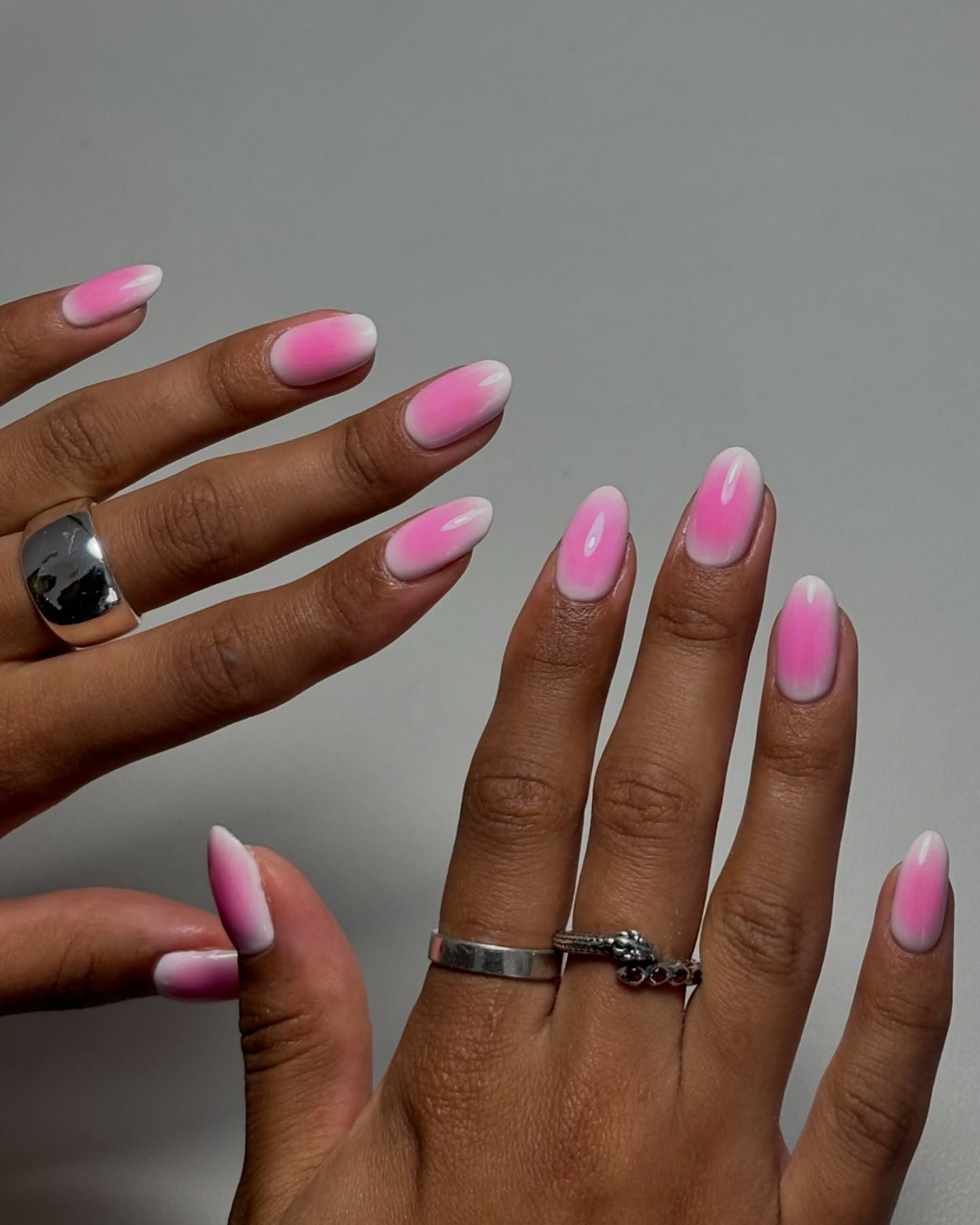Close up of a hand with almond shaped nails with a white background and pink gradient centre.