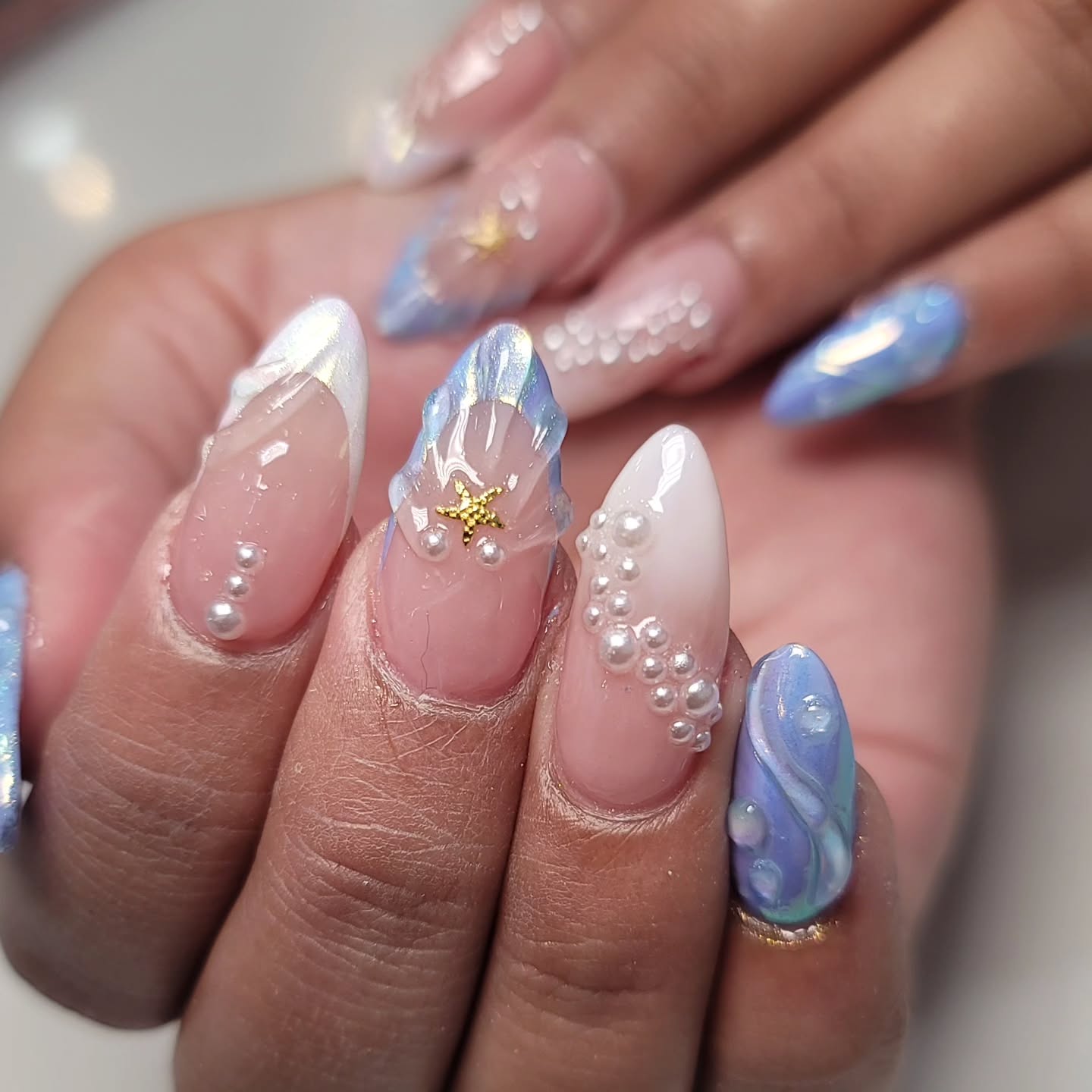 A close up of a hand with almond shaped nails and pearl and shell design