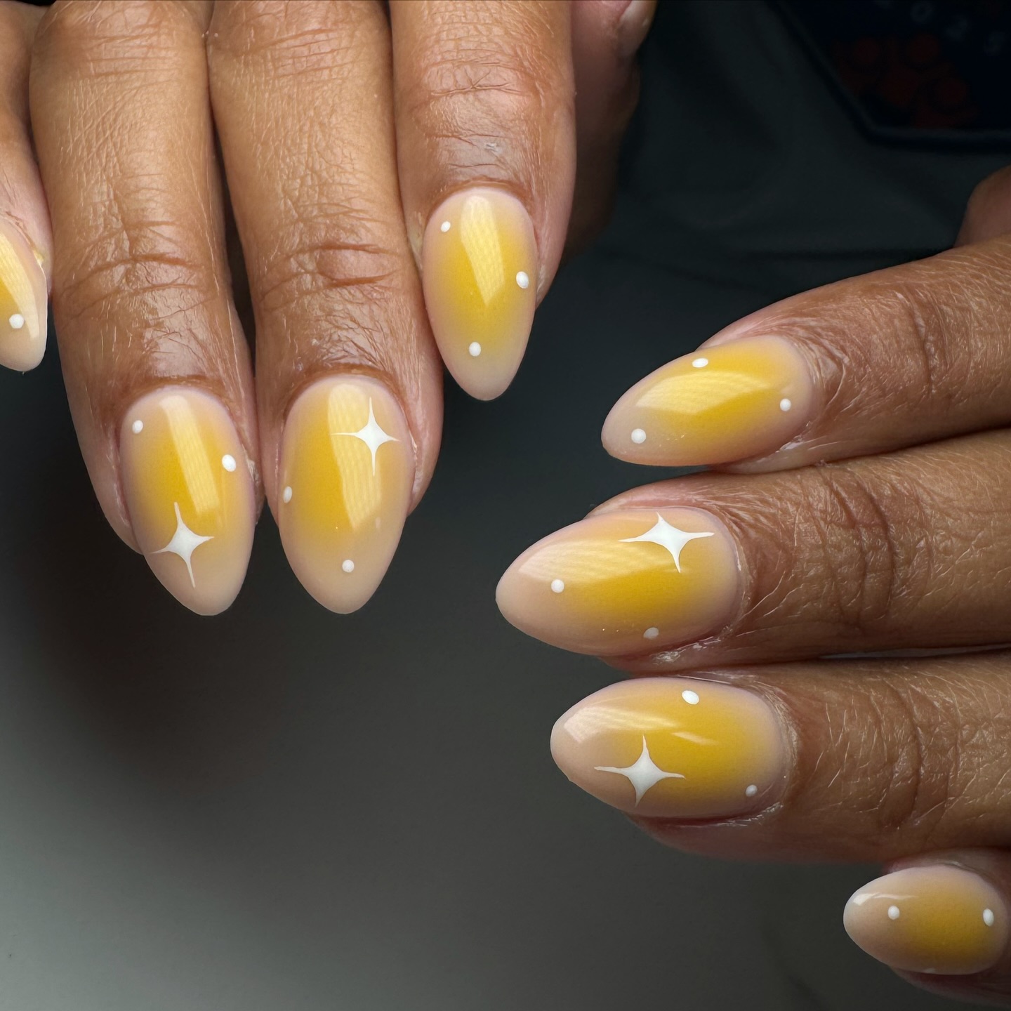 A close up of a hand with almond shaped nails with a beige and yellow base with white sparkle designs
